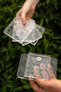A set of clear plastic interchangeable top plates for a soil block drop seeder, held in a person's hands.