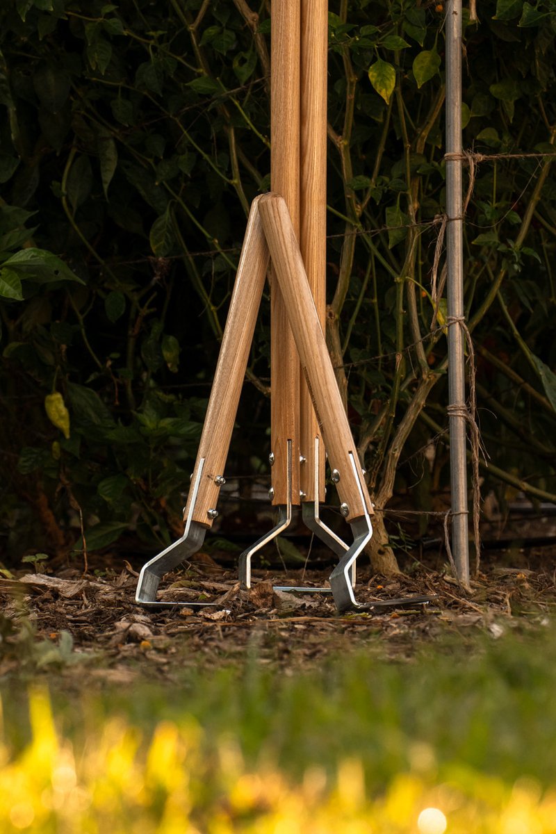 A multifunctional cultivating tool with a wooden handle and a bottom-mounted metal blade, standing upright in the ground.
