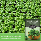 Survival Garden Seeds Corn Salad cold-hardy greens seed packet shown over a close-up photo of growing green lettuce leaves, with text reading 'COLD-HARDY GREENS Thrives when temperatures drop.'.