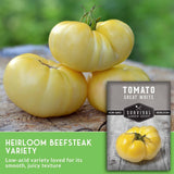 Yellow tomatoes on a wooden surface with a seed packet labeled 'Tomato Great White' from Survival Garden Seeds.