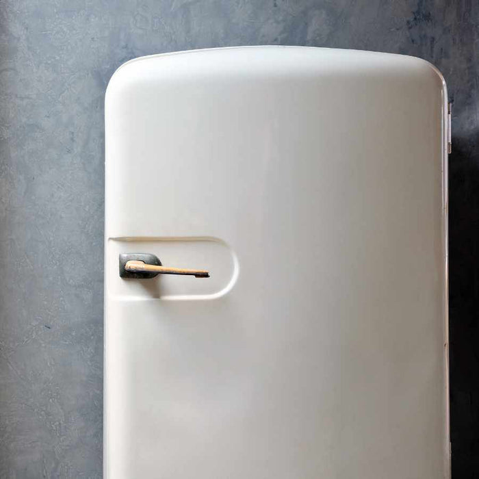White refrigerator with a gold handle against a gray wall